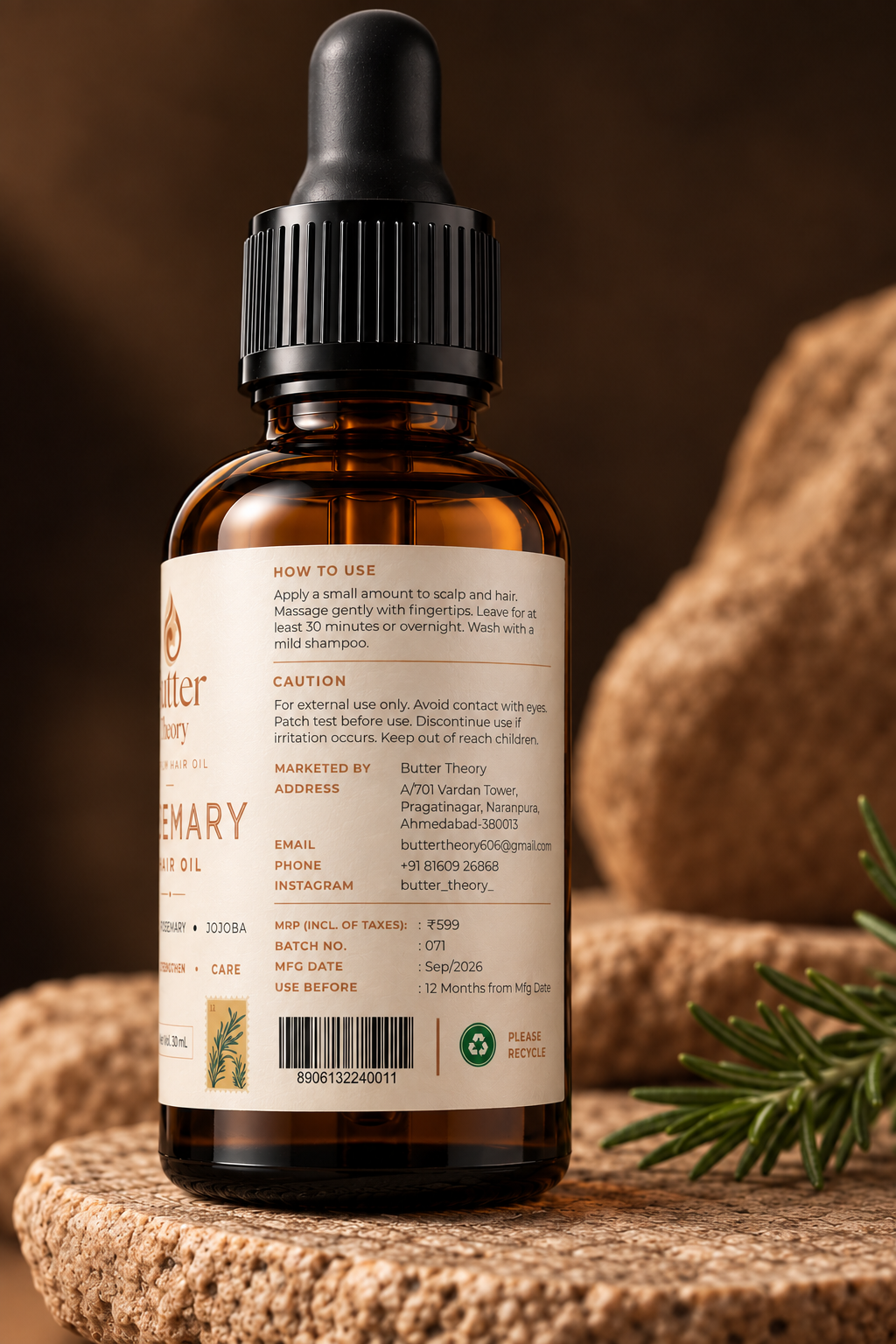 An amber glass dropper bottle of Rosemary Hair Growth Oil shown from the back, featuring a cream-colored label with text and a barcode, set on a rustic wooden surface with a sprig of rosemary and a warm brown background.